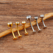 Gold-tone and titanium-tone floating navel barbells with bezel CZ tops and rounded bases on wood.