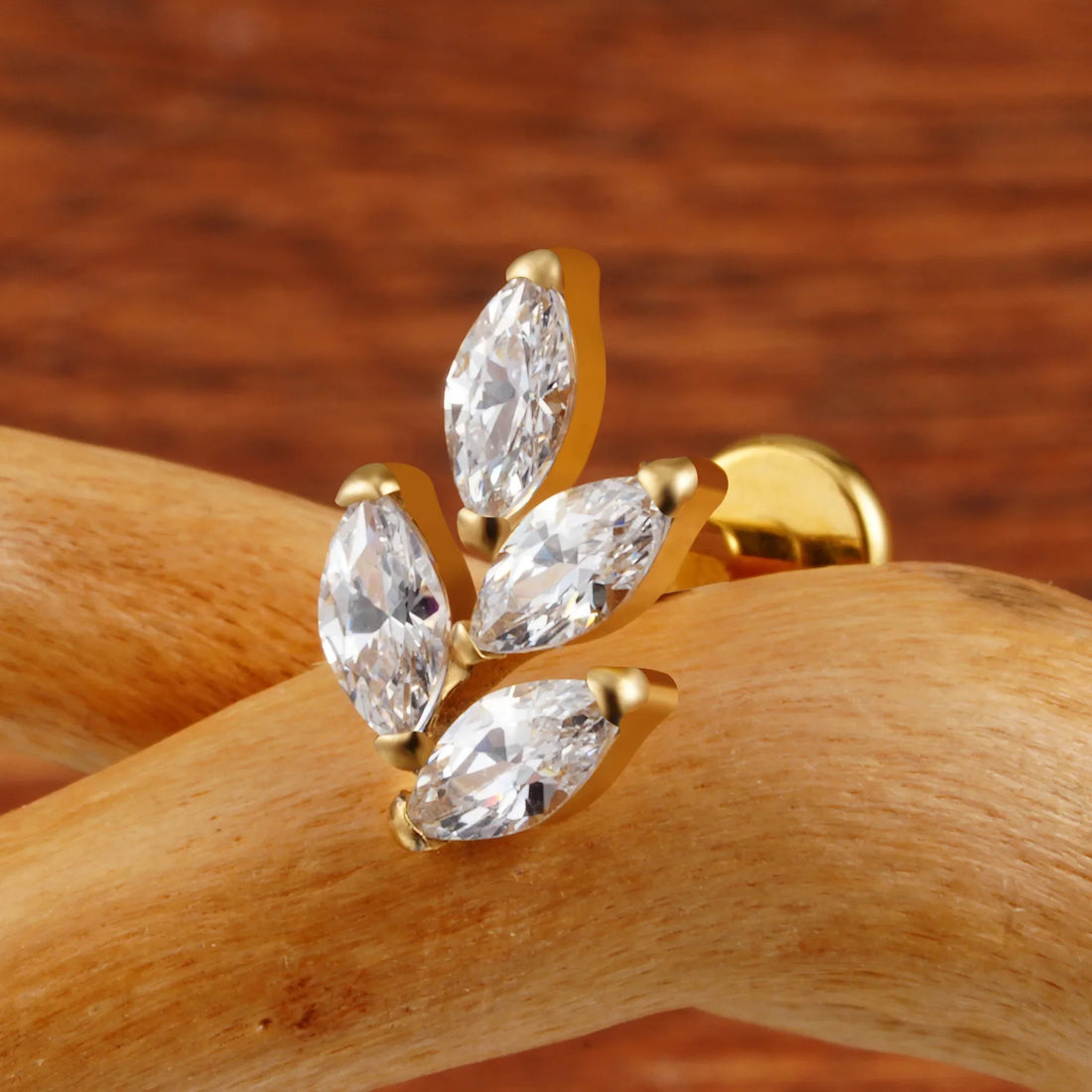 Gold-tone marquise CZ leaf stud photographed close up on a wooden branch.