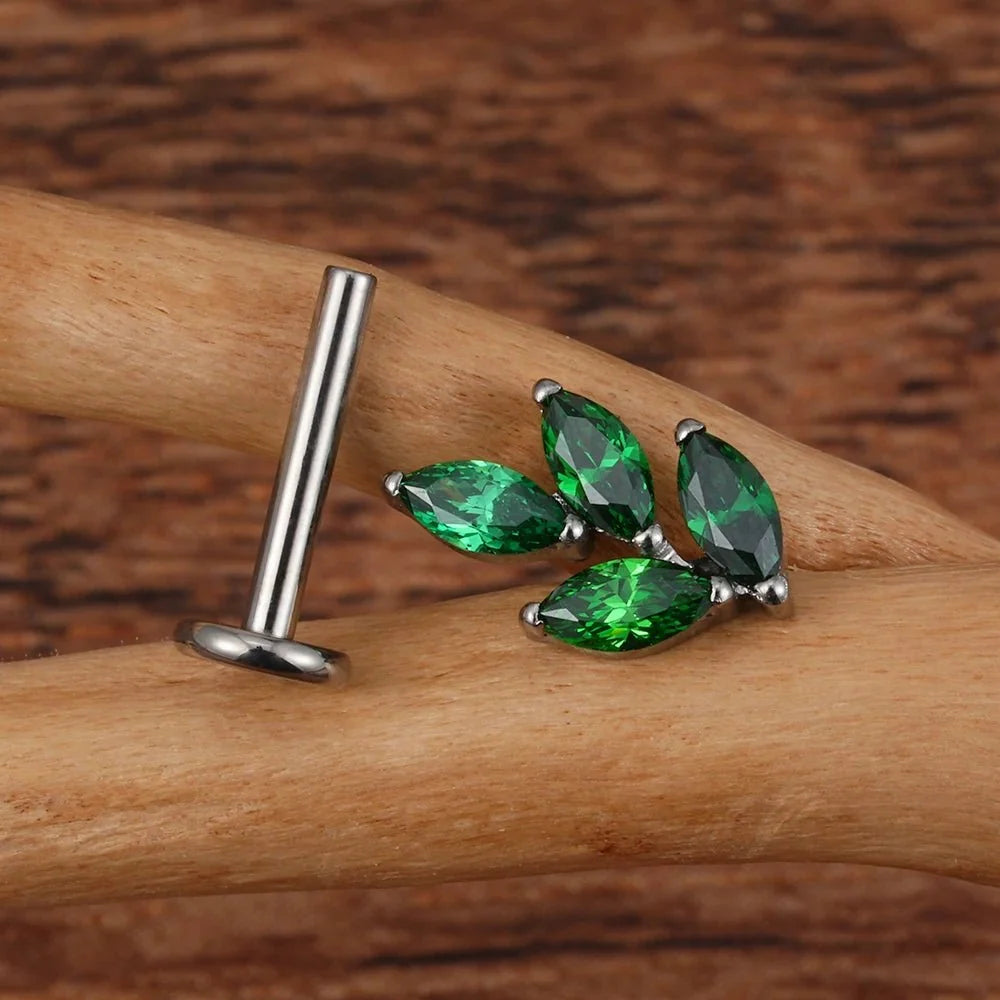 Green marquise leaf top beside a separate silver-tone flat back post on wood.