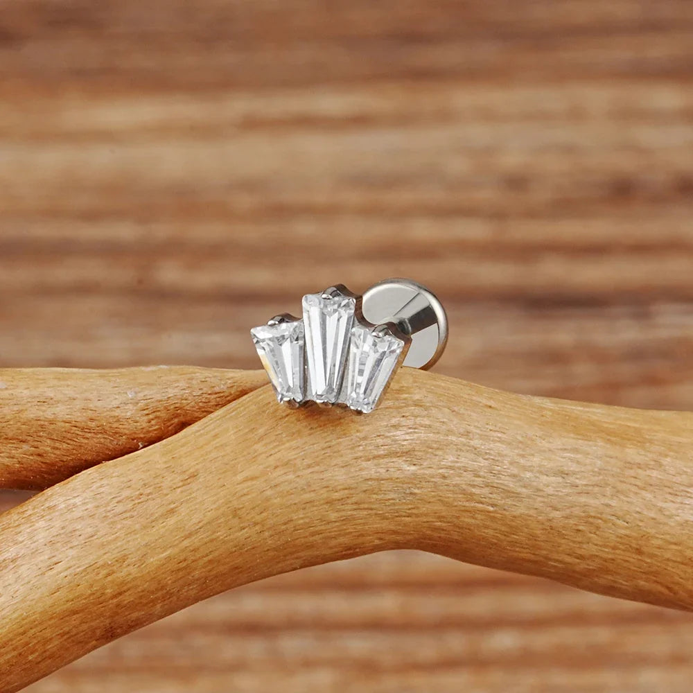 Silver-tone three-baguette CZ crown stud resting on a wooden branch.