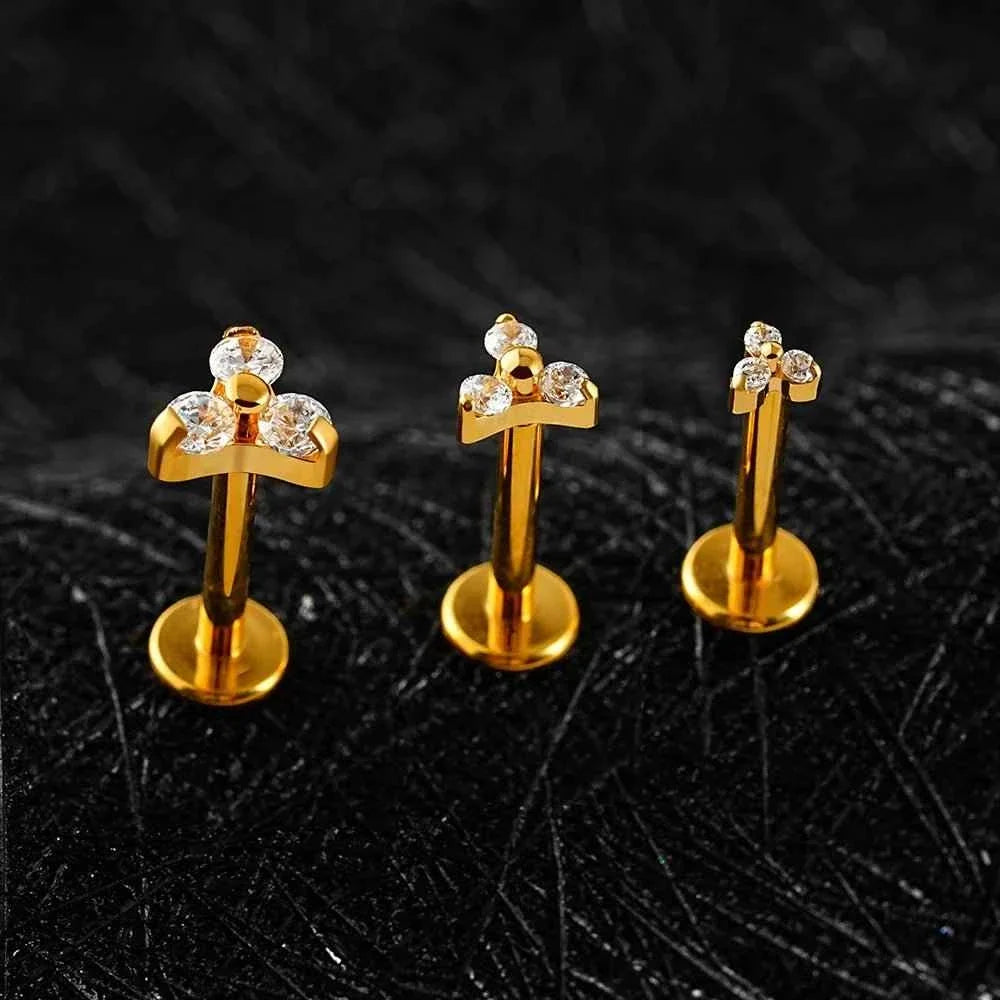 Three gold-tone Trinity CZ flat back studs standing on dark textured stone.