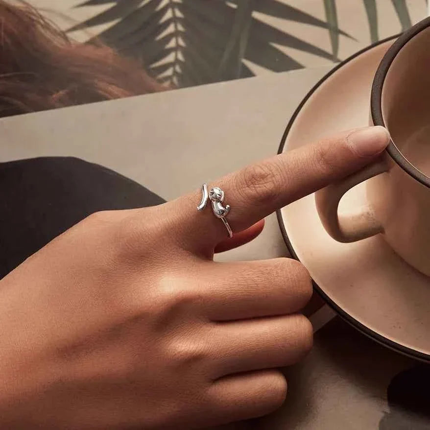 A hand wearing a silver-tone kitten ring beside a cup and saucer.