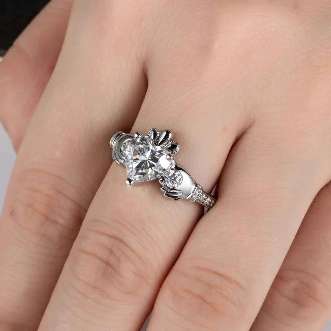 Hand wearing a silver-tone Claddagh ring with a heart-shaped clear moissanite center.