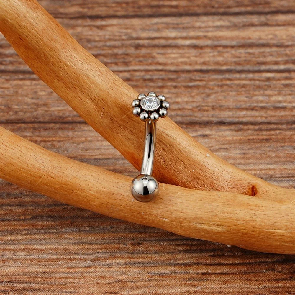 Silver-tone curved barbell with a flower-shaped CZ top and a ball end, photographed on wood.