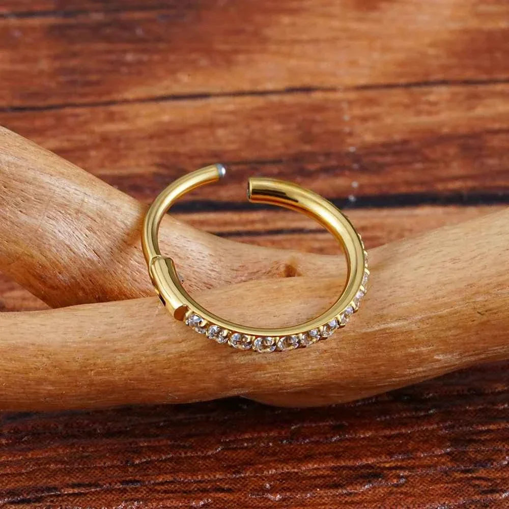 Gold-tone CZ clicker hoop with its hinged segment open, photographed on wood.