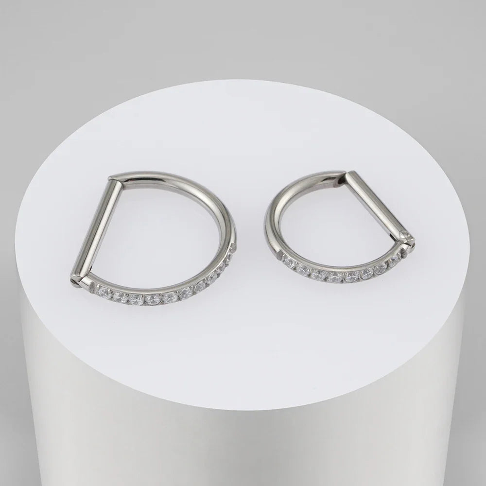 Two silver-tone D-shaped CZ clickers on a white cylindrical display.