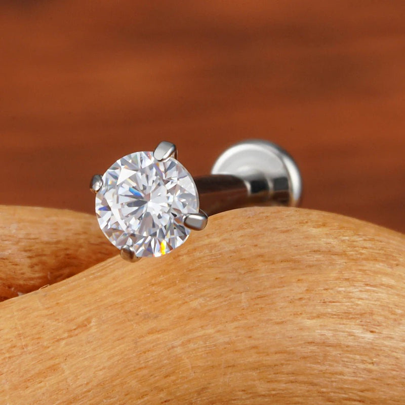 Silver-tone four-prong CZ stud on wood, with its post and flat disc back visible behind the stone.