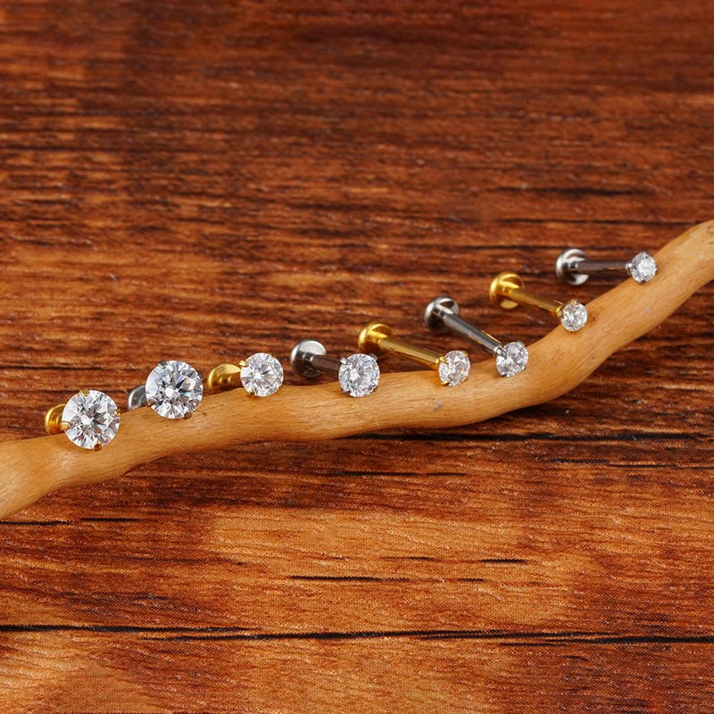 Gold-tone and silver-tone prong-set CZ flat back studs in different sizes arranged along a wooden branch.