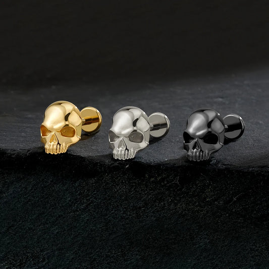 Gold, titanium silver and black skull 16G flat back labret studs on dark background