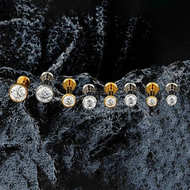 Gold-tone and silver-tone bezel CZ flat back studs arranged on dark textured stone.